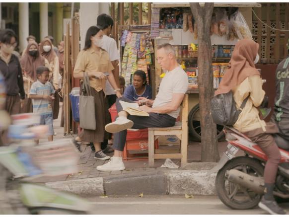 kleurenfoto van presentator Hans Goedkoop zittend op straat in Indonesië