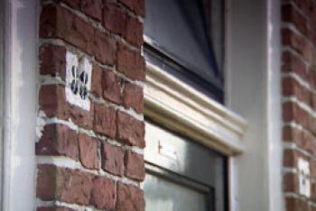 Voorgevel van een bakstenen huis met daarop een huisnummer en een raam. 