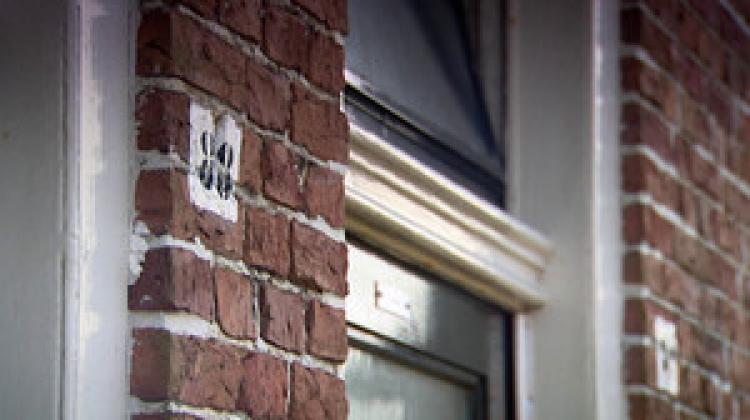 Voorgevel van een bakstenen huis met daarop een huisnummer en een raam. 