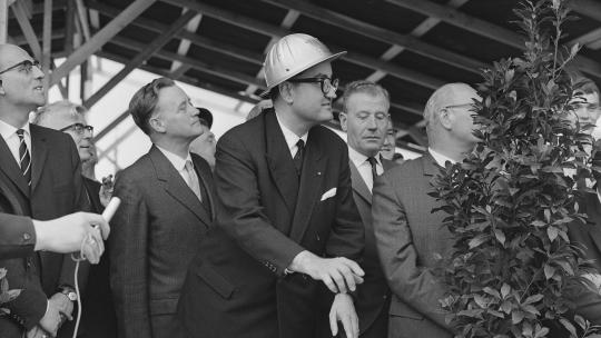 Minister Bogaers met bouwhelm op bedient heimachine